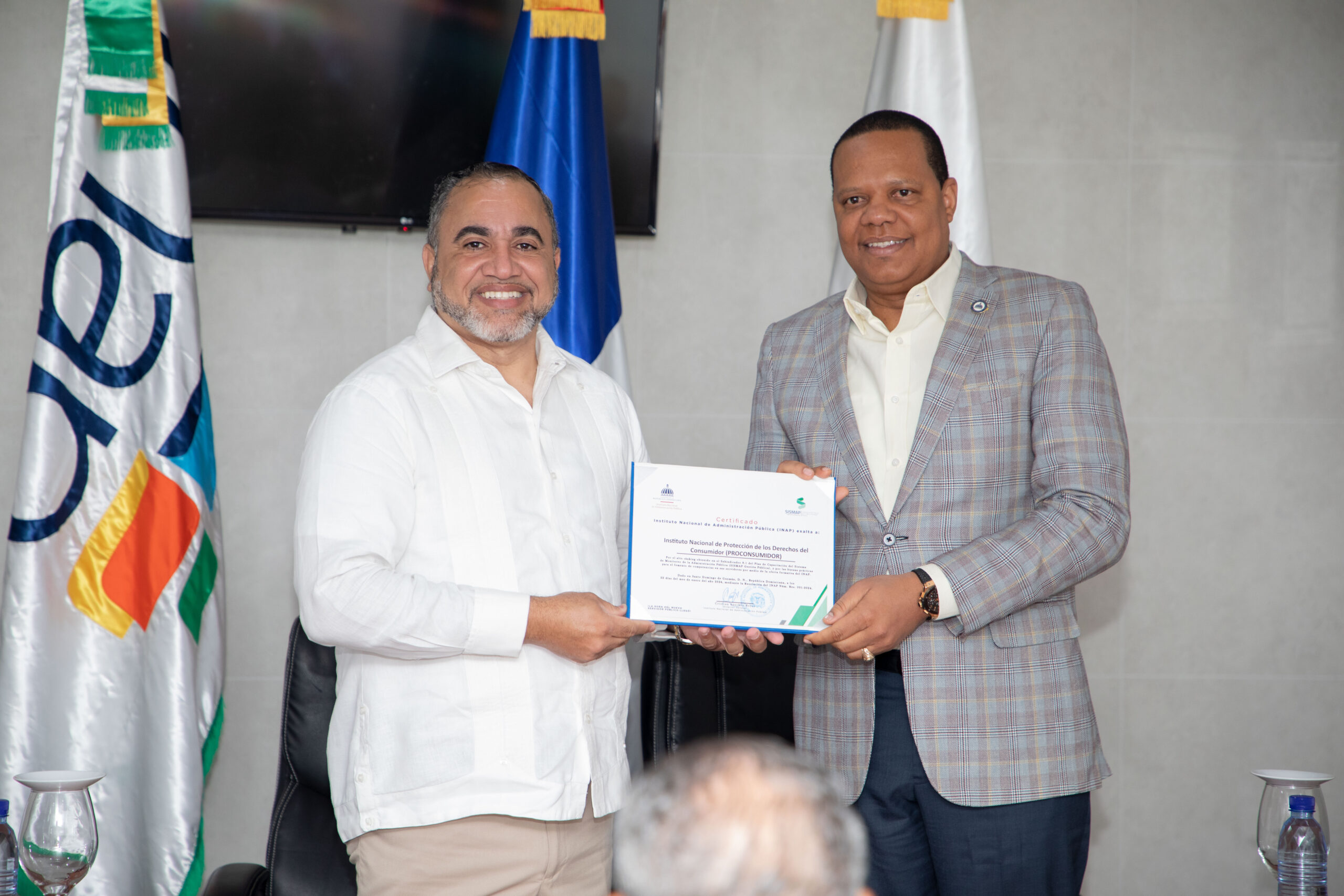 El director ejecutivo de Pro Consumidor, Eddy Alcántara, a la derecha, junto al subdirector del INAP, Ángel Familia, en momento de la entrega del certificado de exaltación.